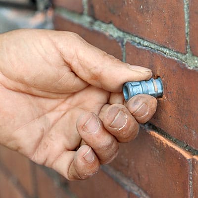 A man sets the anchor for window shutters on a brick house.