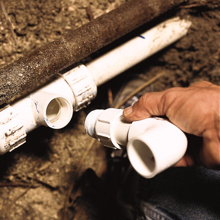 Hands installing PVC tee fitting into main water line connection.