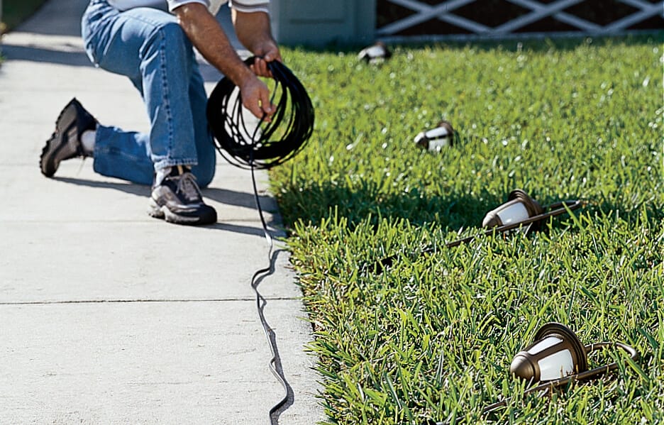 A man lays out landscaping lights and wire.