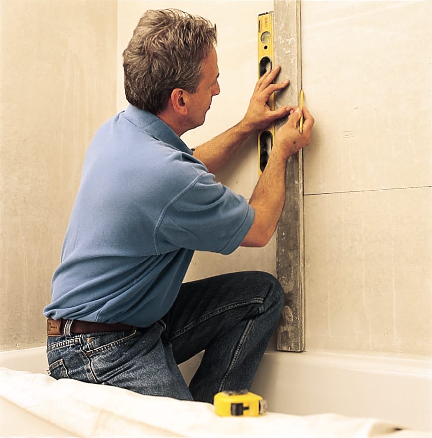a man uses a level and board to mark the area for a tub surround
