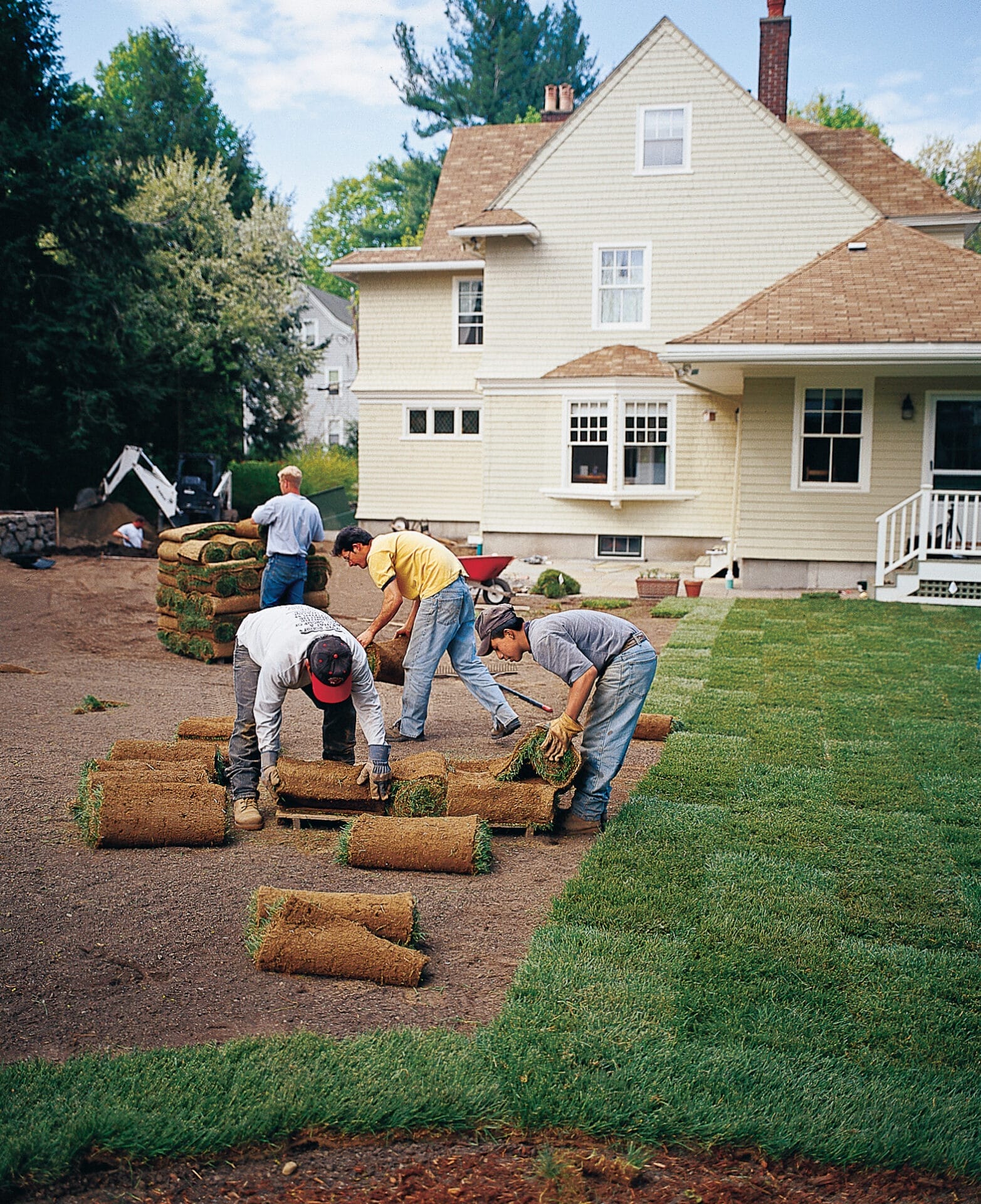 A team of landscapers lay subsequent rows of sod to create a new lawn.