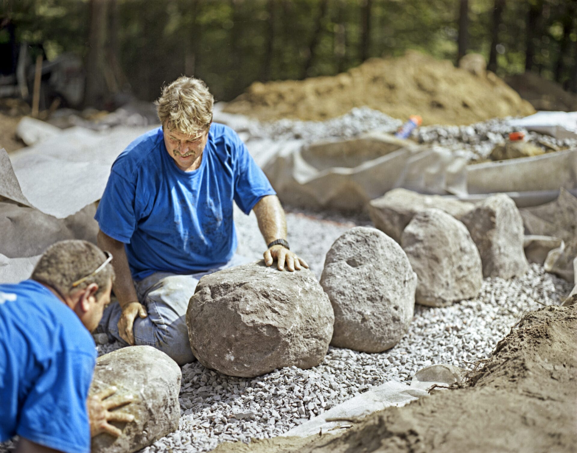 Two men placing the first stones for a stone wall.