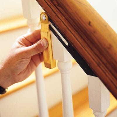 A man measuring a baluster and cutting off excess wood to fit it to the stairwell