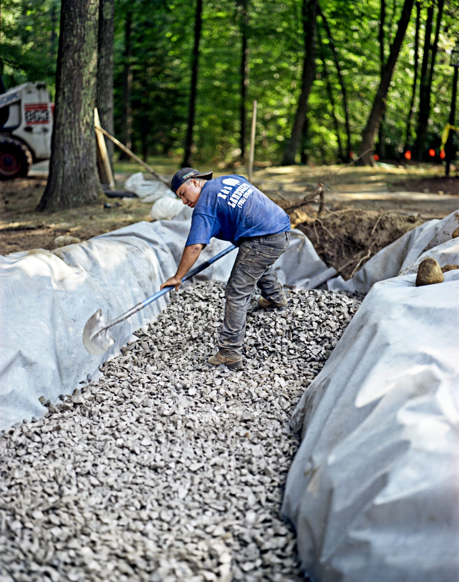 A man shoveling the foundation for a stone wall into a trench.