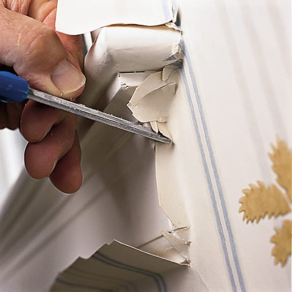 A man trimming newly hung wallpaper around a window apron