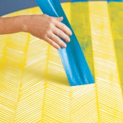A person removing tape from a table with a herringbone pattern painted onto it
