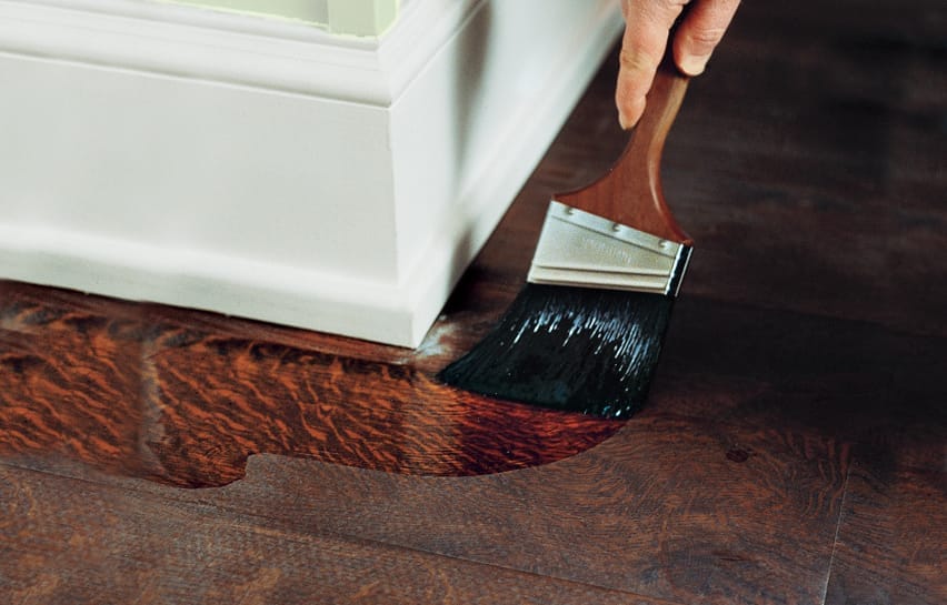 A person uses a paint brush to cut in along the floor edges with the new finish.