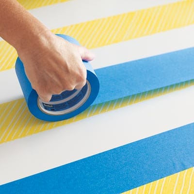 A person removing tape from a table with a herringbone pattern painted onto it