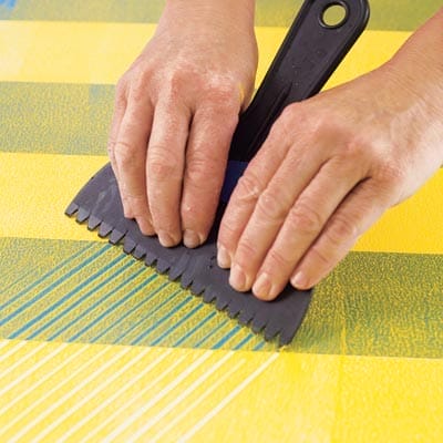A person using a plastic comb to create a herringbone pattern on a table.