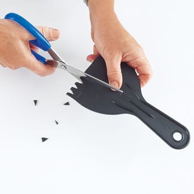 A person cutting a combing tool with a pair of scissors.