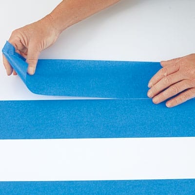 A person applying tape to a table before adding a herringbone pattern.