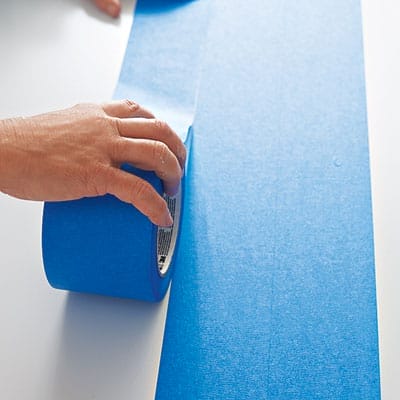 A person applying tape to a table before adding a herringbone pattern.