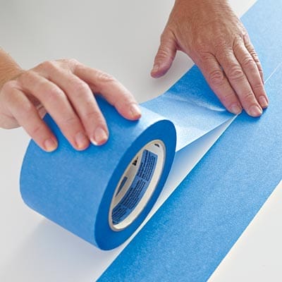 A person applying tape to a table before adding a herringbone pattern.