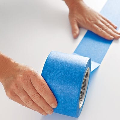 A person applying tape to a table before adding a herringbone pattern.
