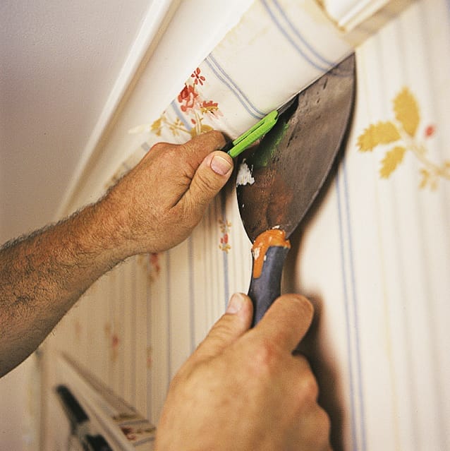 A man trimming the edges of a wallpaper so that it fits the wall snugly.