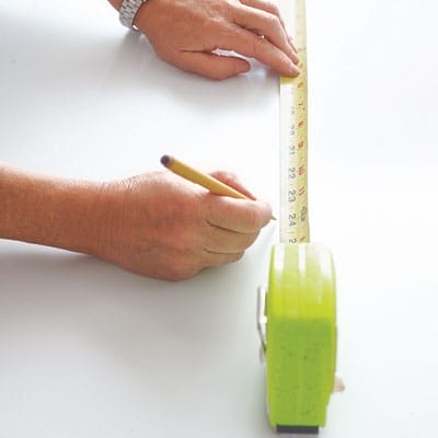 A person measuring and marking a table for a herringbone pattern.