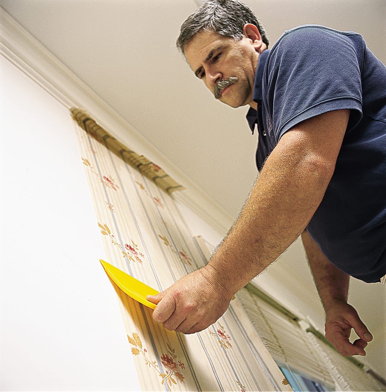 A man hanging the first strip of a new wallpaper on a wall.