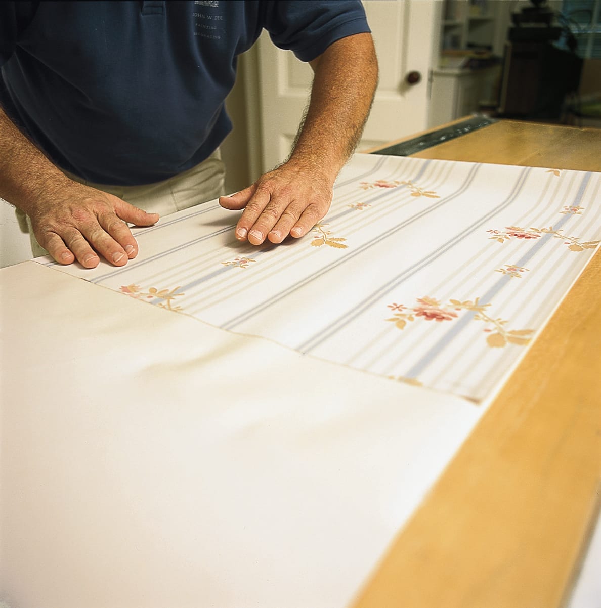 A man smoothing wallpaper flat against a table