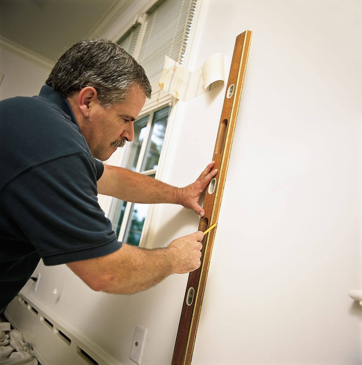 A man taking measurements and marking a wall in preparation of putting up wallpaper