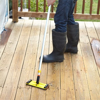 A man wearing boots sanding a wooden deck.
