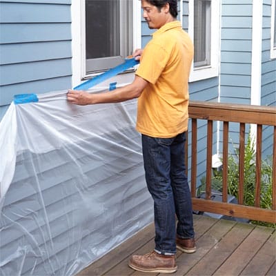 A man taping up plastic sheeting to cover house siding.