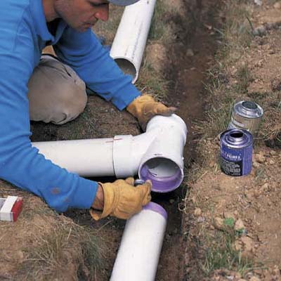 Man installing gutter downspout extension glues a T-fitting to the pipe in the trench.