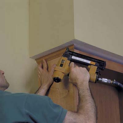 A man using a drill to secure a bookcase to the ceiling.