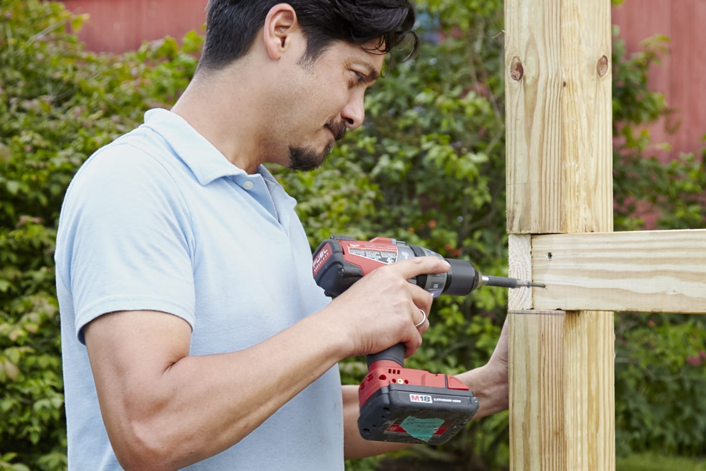 A person attaching the rails of a garden fence to their posts.