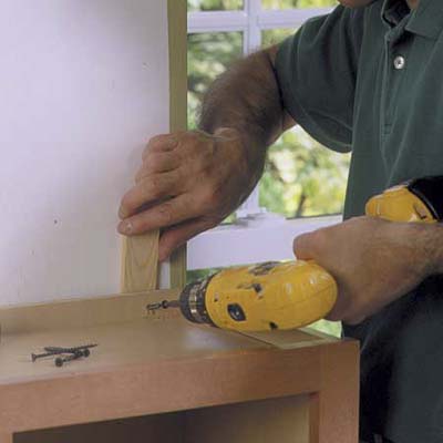 A man using a drill and screws to fasten a cabinet to a wall.