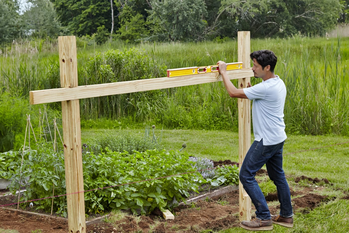 A person using a level to help set a post for a garden fence.