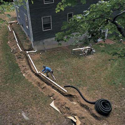 Man installing gutter downspout extension lays out pipe lengths and fittings along side the trench he dug.
