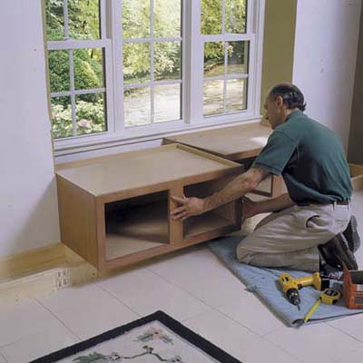 A man pushing cabinets beneath a window to create a window seat.
