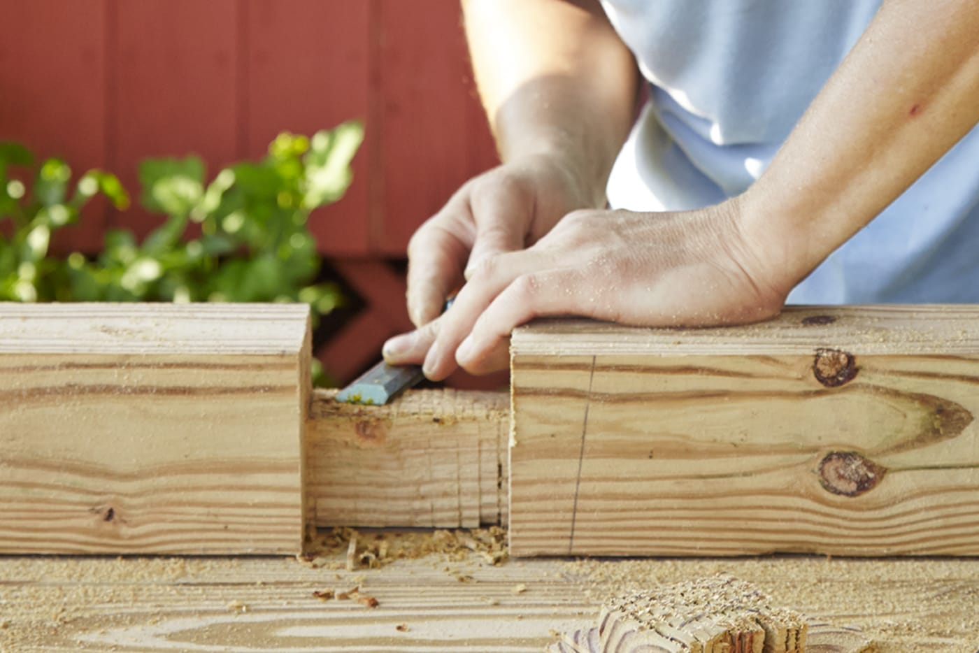 A person cutting notches into posts for a garden fence.