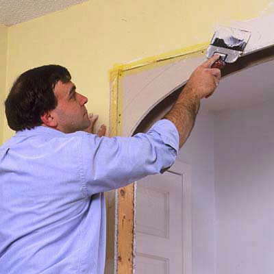 A man tapes and compounds the drywall seams from the drywall extension used to create an archway.