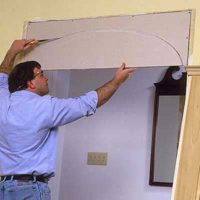 A man cuts out the drywall arch he just traced to reveal an archway.