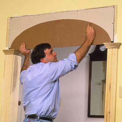 A man traces an arch stencil onto the drywall extension to create the arch.