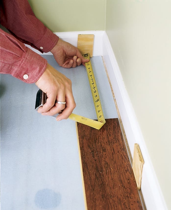 installing the first row of wood planks against a wall but leaving enough space for trim to be added