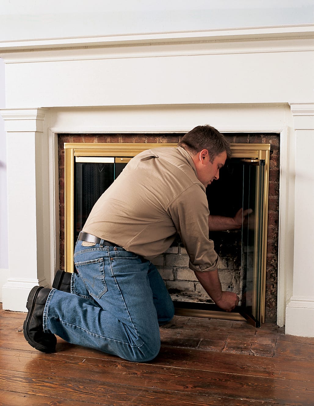 A man marks glass fireplace doors with screw holes.