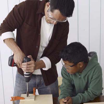 A child watches a man cut tool holders for the toolbox.