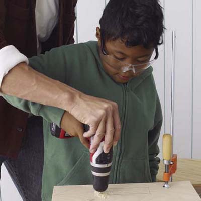 An adult helps a child drill holes for the toolbox handle.