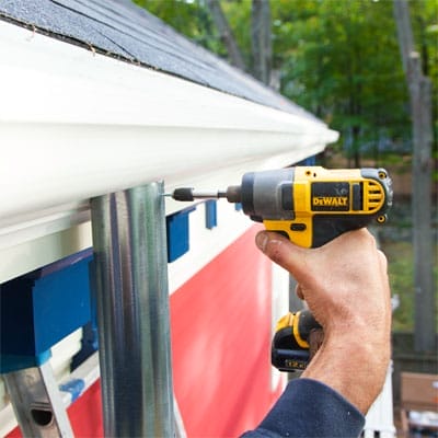 A drill being used to install downspouts for a fiberglass gutter.