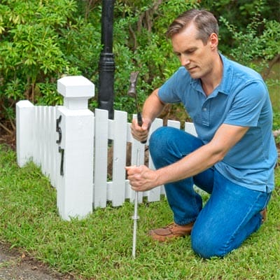 A man using a hammer to install the rod of a driveway marker.