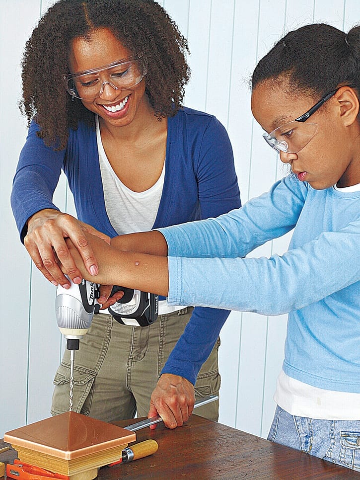 Two people using a drill to prepare the top of a bird feeder for wiring.
