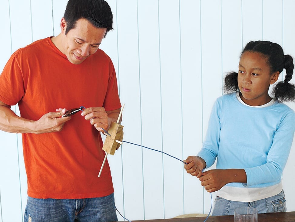 Two people running a wire through the base of a bird feeder.