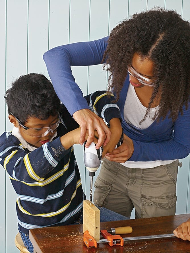 Two people using a drill to create the base of a bird feeder.