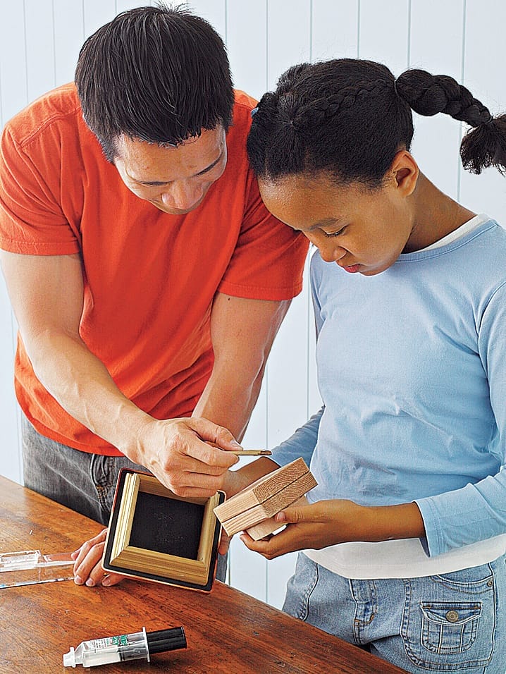 Two people constructing the top of a wooden bird feeder.