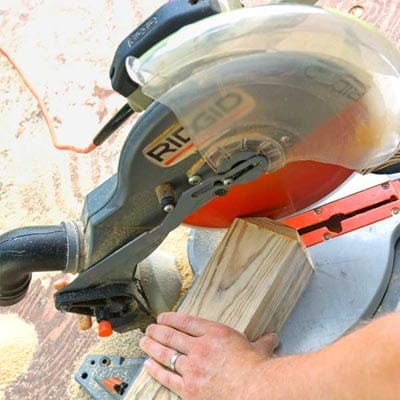 A miter saw being used to cut the end of a post for a driveway marker.