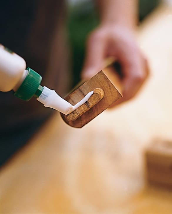 Hand applying waterproof glue to wooden tenon joint with squeeze bottle.