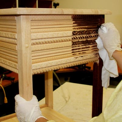 A person applying stain to the trim of a table.