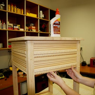A person applying trim to the side of a table